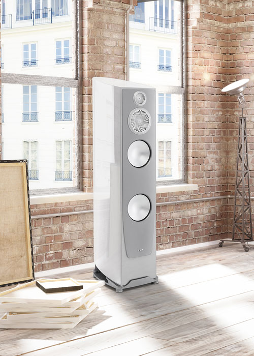 A floorstanding loudspeaker in a brick room.