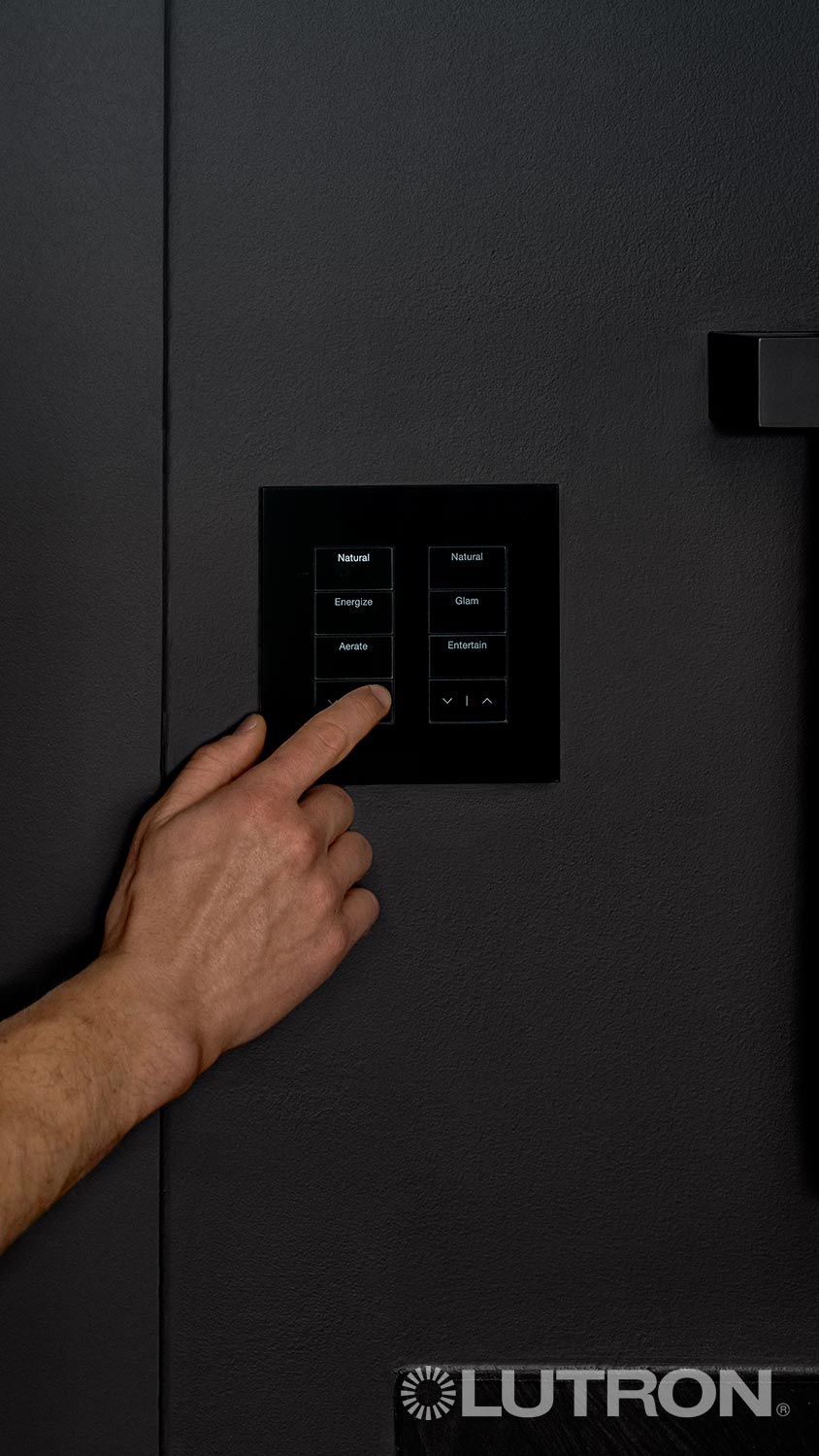 Hand pressing a lighting control panel labeled Lutron