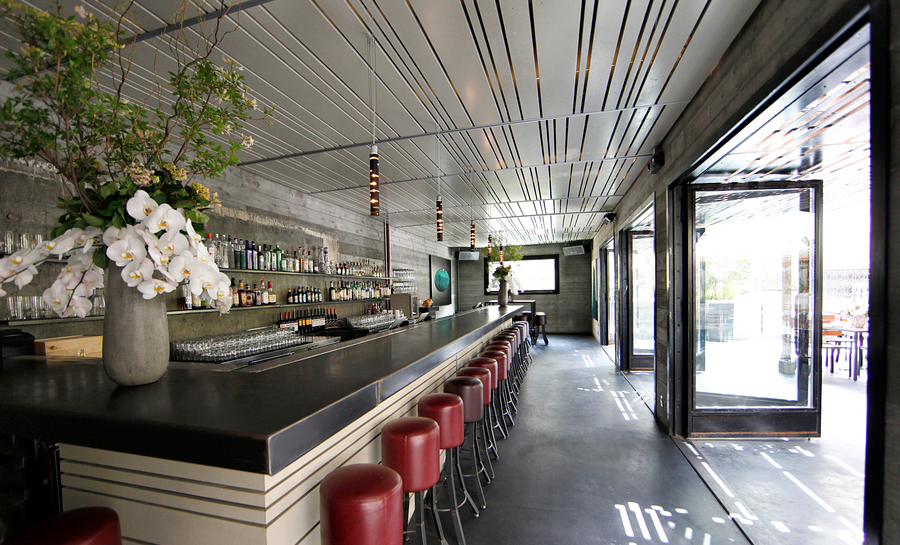 A bar with large, open doors, red stools, and a vase of flowers on the counter.