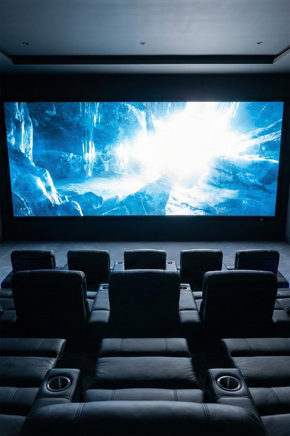 Modern home theater with multiple rows of black leather recliners facing a large bright screen