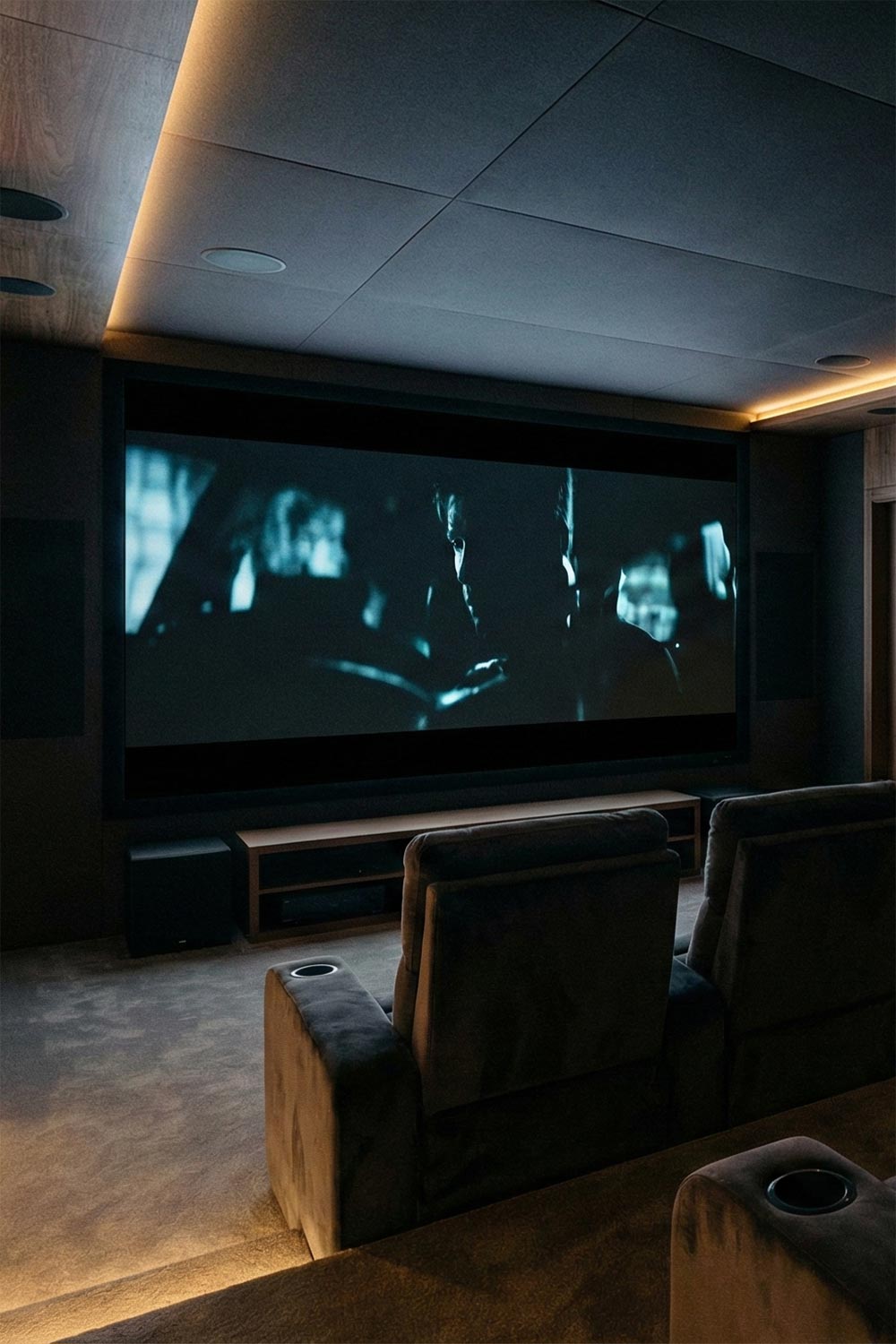 Home theater room with plush grey seating and warm recessed cove lighting on the ceiling