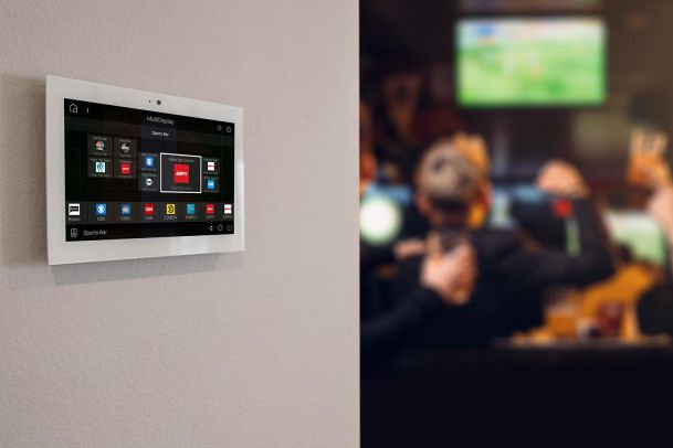 Wall-mounted smart control panel in sports bar with screens in background