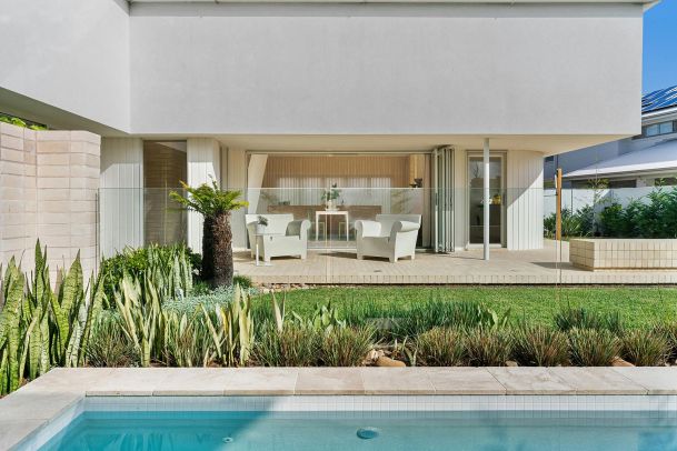 Outdoor patio with white chairs and table overlooking garden and pool